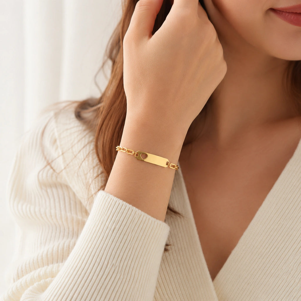 A close-up lifestyle shot of a woman wearing a gold-plated ID bracelet on her wrist, paired with a cream-colored ribbed knit cardigan.