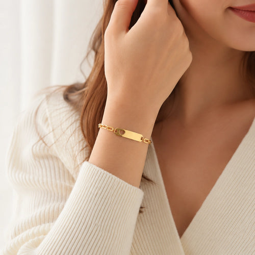 A close-up lifestyle shot of a woman wearing a gold-plated ID bracelet on her wrist, paired with a cream-colored ribbed knit cardigan.