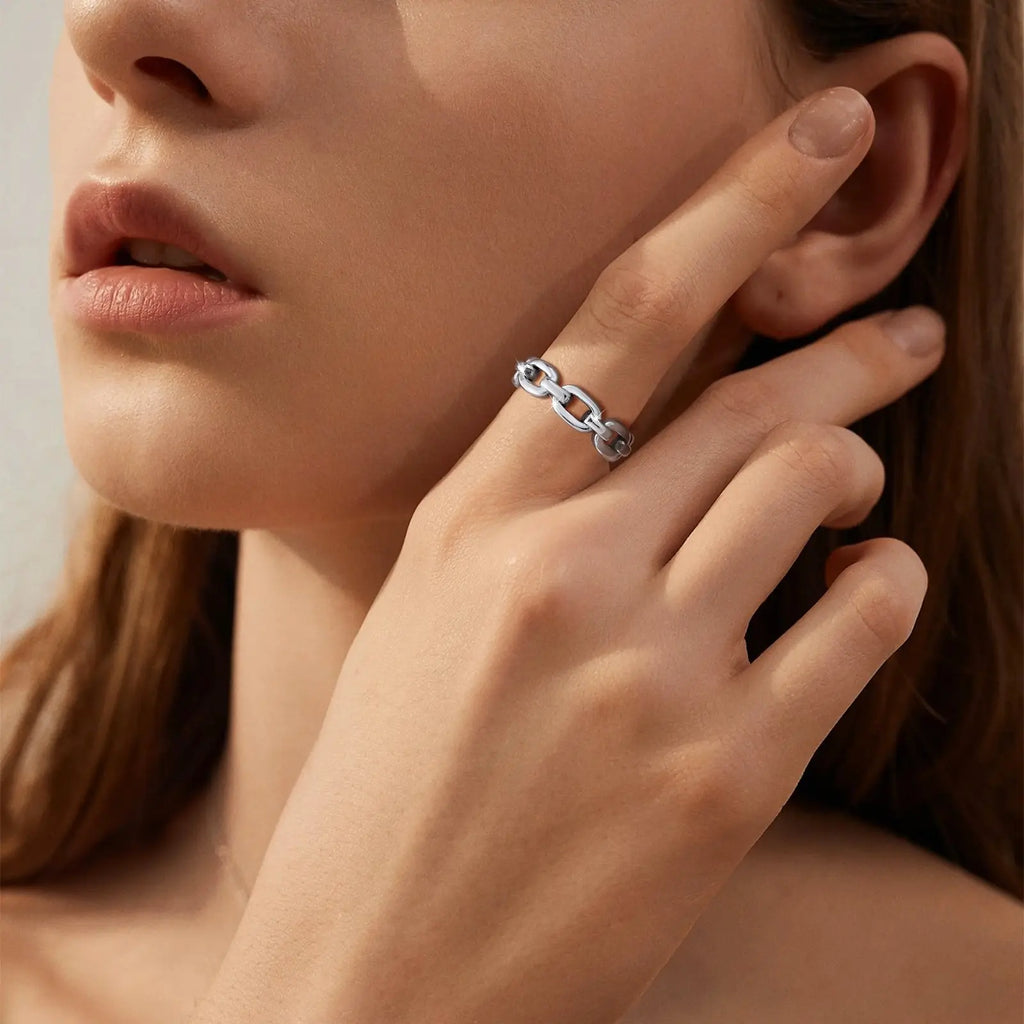 Close-up of a woman's hand wearing a silver chain-link ring, touching her face.