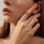 Close-up of a woman's hand wearing a silver chain-link ring, touching her face.