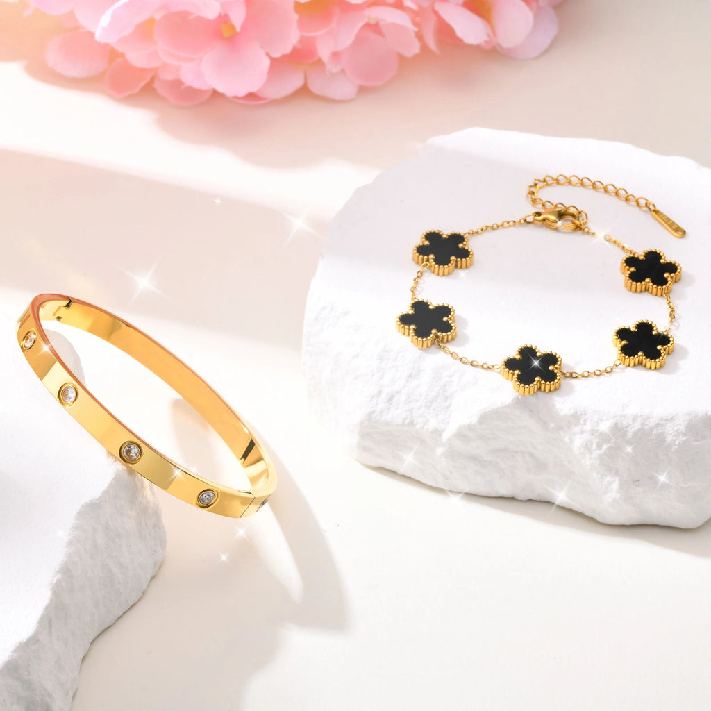 Black acrylic flower bracelet and gold tone crystal bangle displayed on white jewelry props with pink flowers in the background.