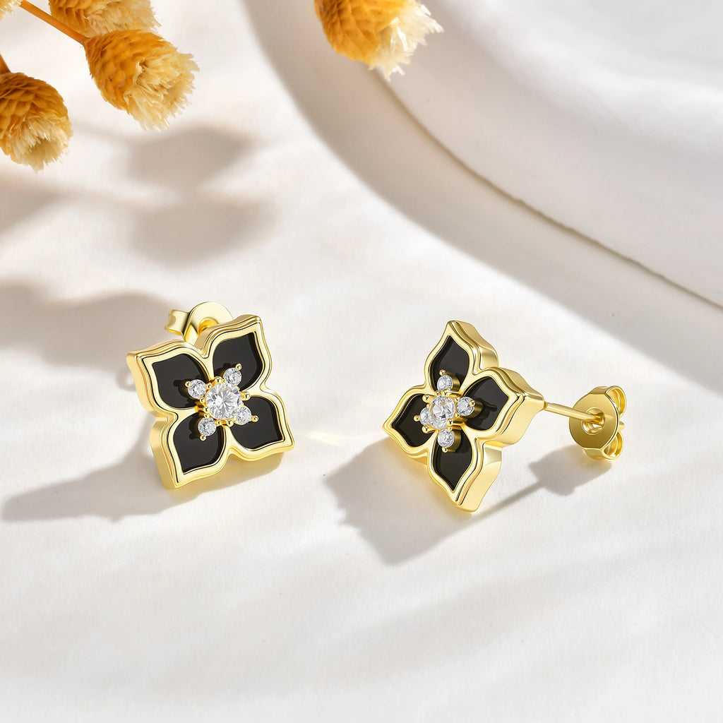 Pair of black and gold floral stud earrings with sparkling cubic zirconia stones displayed on a white surface with yellow flowers.