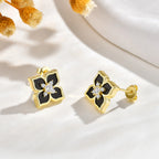 Pair of black and gold floral stud earrings with sparkling cubic zirconia stones displayed on a white surface with yellow flowers.