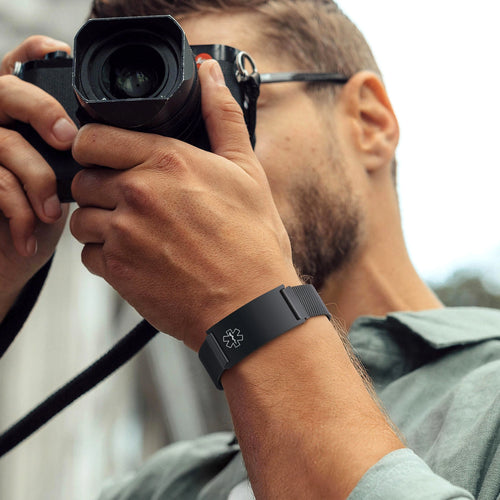 Person wearing a black stainless steel mesh medical ID bracelet with an adjustable magnetic clasp.