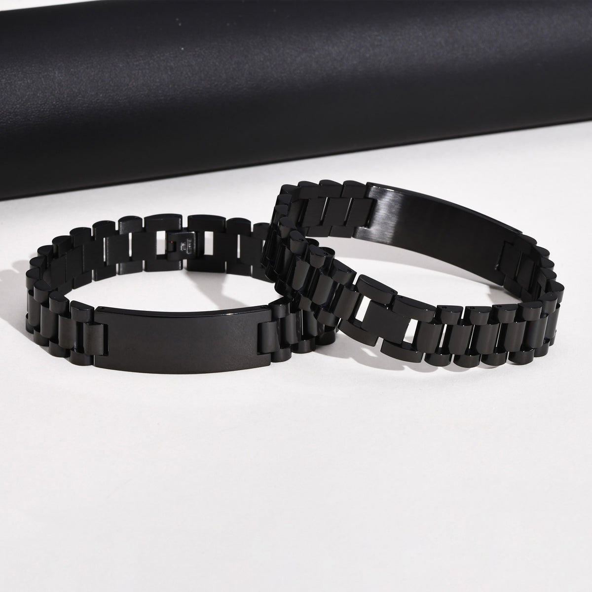 Two views of a black stainless steel bracelet featuring classic metal links and a curved ID plate