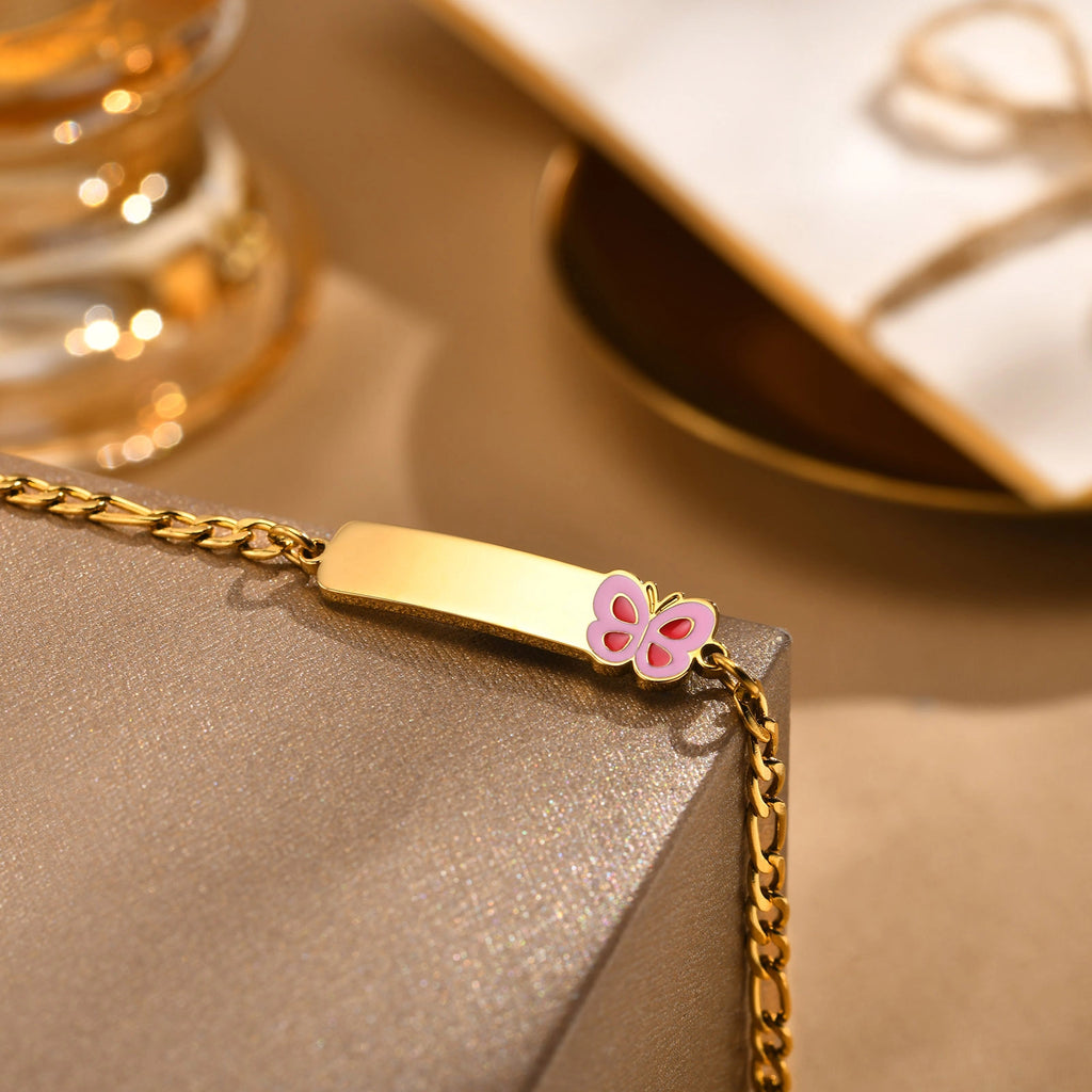 Close-up of a gold kids medical ID bracelet showing the polished engraving plate and pink butterfly design.