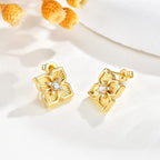 Pair of gold four leaf clover CZ stud earrings displayed on a white surface with delicate yellow floral accents.