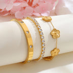 Gold tone floral bracelet stack displayed on a white jewelry stand beside pink flowers, featuring gold flower charms, a CZ tennis bracelet, and a crystal bangle.