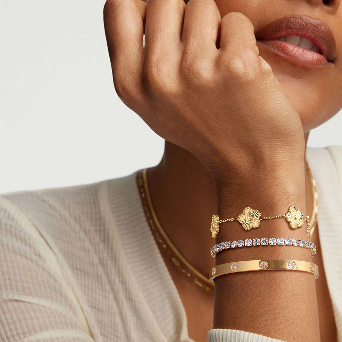 Close-up of a model wearing layered gold tone bracelets with textured gold flower charms, a sparkling CZ tennis bracelet, and a polished bangle.