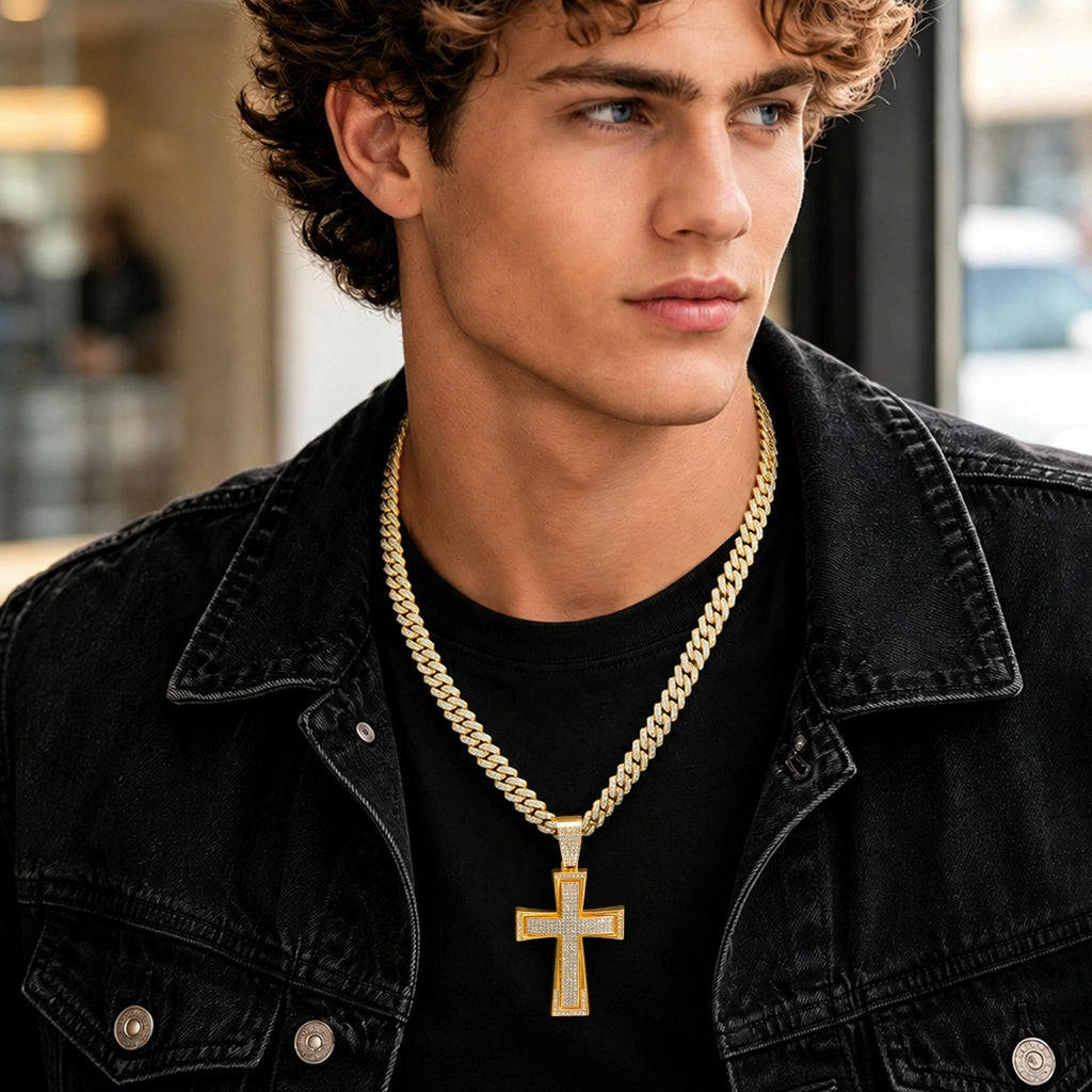 Male model wearing a gold tone Cuban link chain necklace with a large sparkling cross pendant, styled with a black denim jacket.
