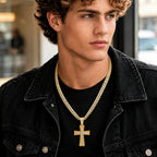 Male model wearing a gold tone Cuban link chain necklace with a large sparkling cross pendant, styled with a black denim jacket.