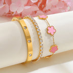Pink and gold floral bracelet set displayed on a white jewelry stand beside pink flowers, featuring a pink acrylic flower bracelet, CZ tennis bracelet, and crystal bangle.