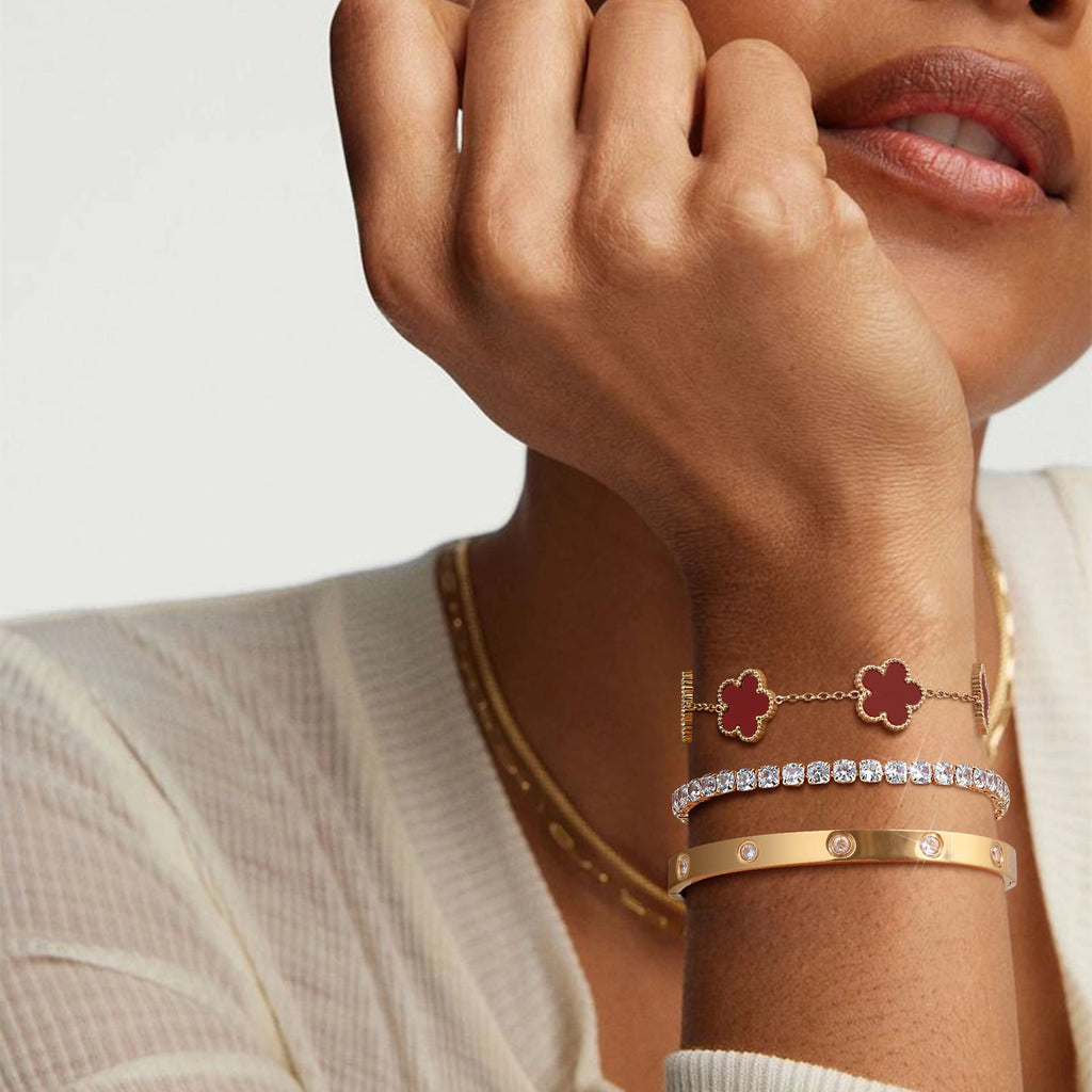 Close-up of a model wearing layered gold tone bracelets with red floral charms, sparkling cubic zirconia stones, and a polished crystal bangle.