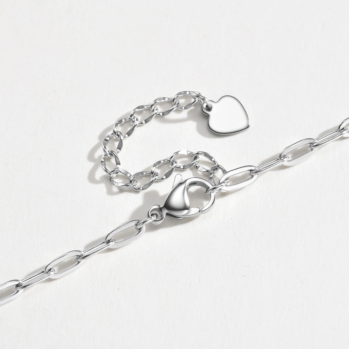 A silver paperclip chain necklace with a lobster clasp and a small heart-shaped charm, displayed on a clean white background.