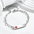 A silver-tone ID bracelet featuring a flat bar engraved with a red medical star of life symbol and a small clear rhinestone, displayed on a clean white surface with decorative white columns.