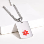 Silver medical ID dog tag necklace displayed on a white surface with the red medical alert symbol visible.